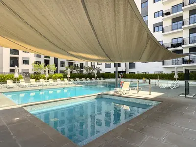 a large swimming pool with a large umbrella over it at Modern & Cozy 2BR Apartment at The Nook 1 Near Metro in Dubai