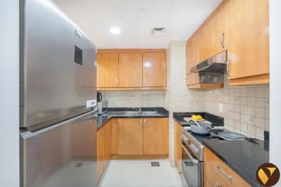 a kitchen with wooden cabinets and a stainless steel refrigerator at Vogue JLT Global Lake View Tower near Marina and JBR, Two Bedroom Apartment with Balcony and City view, Access to all Amenities in Dubai