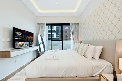 a white bedroom with a large bed and a tv at Bloomfields Grandeur 2BR in Azizi Riviera in Dubai