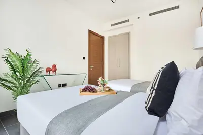 a white bedroom with two beds and a plant at Frank Porter - The Crest Tower, Sobha Hartland in Dubai