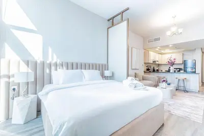 a white bedroom with a large bed and a kitchen at Stylish Studio in JVC with Pool and Gym Access in Dubai