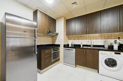 a kitchen with wooden cabinets and a stainless steel refrigerator at Cozy 1BR Apartment at Elite Residence Dubai Marina in Dubai