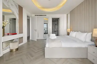 a white bedroom with a large bed and a living room at BurjKhalifaViews,1BHK, High Floor, Damac Paramount Tower B in Dubai