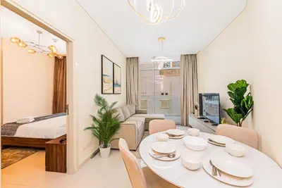 a living room with a white table and a room with a bed at Escape 24 Stylish 1BR in Artesia, Pool & Gym, Damac Hills in Dubai