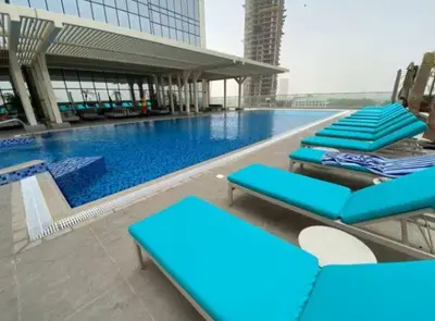 a swimming pool with blue lounge chairs in front of a building at Vogue JVT Novotel Near Springs Souk Mall, One Bedroom Apartment with Large Balcony and Vibrant Community view, Access to all Amenities in Dubai