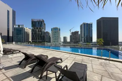a swimming pool with chairs and a city skyline at Modern Smart & Spacious 1BR Business Bay near Downtown Dubai in Dubai