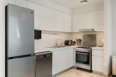a kitchen with white cabinets and a stainless steel refrigerator at Premium 2BR with Park View in Dubai Creek Harbour in Dubai