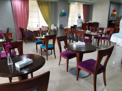 a restaurant with tables and purple chairs and a chef in the background at Al Manar Grand Hotel Apartment in Dubai