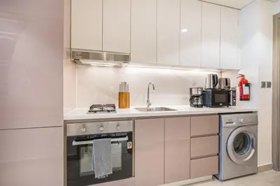 a white kitchen with a sink and a dishwasher at Modern Luxe Studio in the Heart of Meydan in Dubai