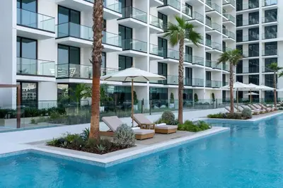 a swimming pool with chairs and umbrellas in front of a building at Binghatti Phoenix Luxe 1BR with Tranquil Pool View in Dubai