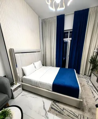 a bedroom with a large bed in a room with blue curtains at Modern Studio in Opalz - Ideal for Work & Leisure in Dubai