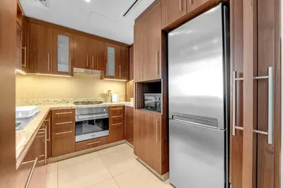 a kitchen with wooden cabinets and a stainless steel refrigerator at Waves - Luxury 2BR Apt With Burj Khalifa & Fountain View in Dubai