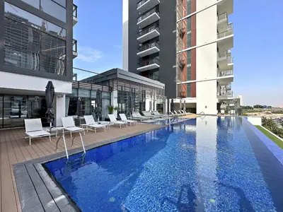 a swimming pool with white chairs and a building at VayK - Ideal Studio in Sobha Hartland in Dubai