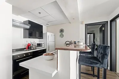 a white kitchen with a counter and chairs in it at VayK - Modern 1BR Near Metro in Dubai Marina in Dubai