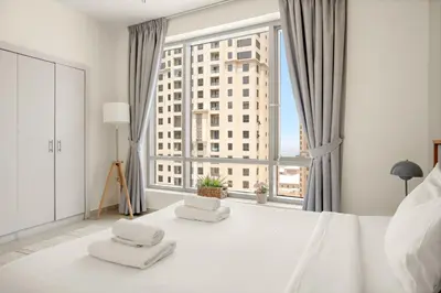 a white bed with two white stools in front of a window at VayK - Inviting 1BR in Dubai Marina with Stunning Views in Dubai