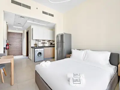 a bedroom with a large white bed and a kitchen at Trendy Luxe Studio In Al Furjan close to Metro-17 in Dubai