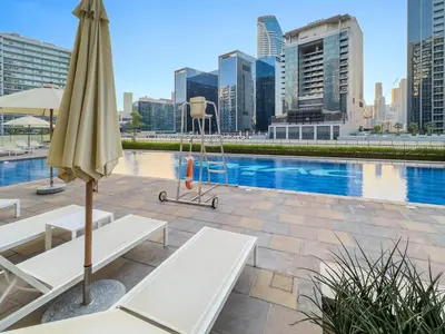 an umbrella and chairs next to a pool with buildings at Reva Residence Comfort Suite 1BDR Plus Sofa Bed in Dubai