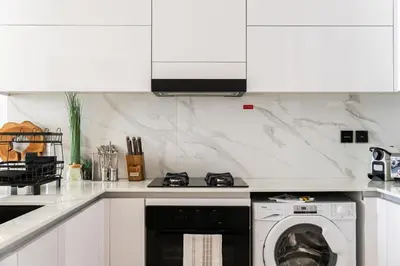 a white kitchen with a washer and a stove at SettlerHomes - JVC Skyline Views - Pool & Gym in Dubai