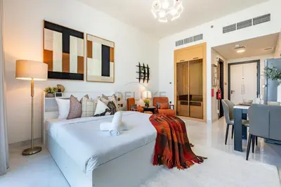 a bedroom with a large white bed and a dining room at Peaceful High-Rise Studio Overlooking Miracle Garden, Skyz by Danube, Arjan by Deluxe Holiday Homes in Dubai
