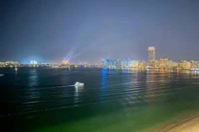 a view of a city from the water at night at Miami Vibes - 1BR with Private Beach, Sea, Palm View in Dubai