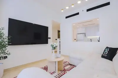 a white living room with a large tv on a wall at Prime 2BR in Binghatti Crest - JVC in Dubai