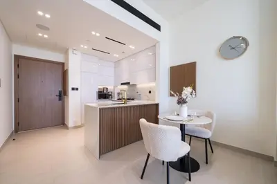 a kitchen with a table and chairs and a clock at High Floor JVC 1BR Skyline Showstopper in Dubai