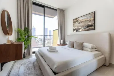 a white bedroom with a bed and a large window at GuestReady - Cozy Stay | Near Parks | JVC in Dubai