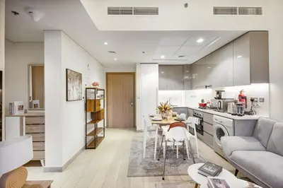 a kitchen and living room with a table and a couch at Cozy 1BR with Pool & Gym l 15mn to Downtown in Dubai