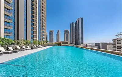 a large swimming pool with chairs and buildings at Designer 1BR Dubai Creek Harbour in Dubai