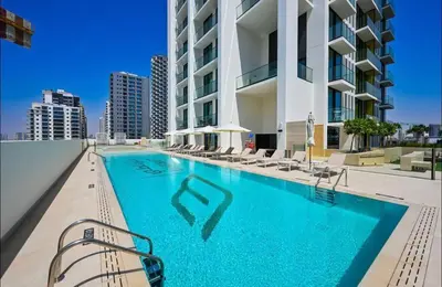 a swimming pool with chairs and a building at Studio in JVC I Pool View I Near Mall & Dining in Dubai