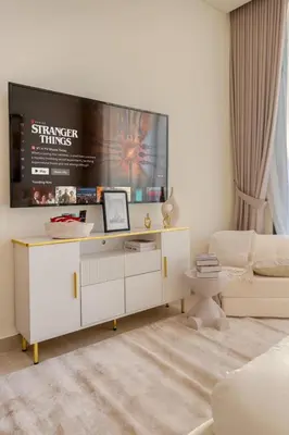 a white living room with a large tv on the wall at Cozy JVC Studio I Pool & Gym I Fully Furnished in Dubai