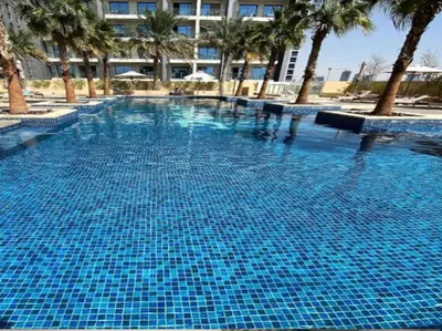 a large blue swimming pool with palm trees and a building at Exquisite Lavish Studio in Ghalia JVC -16 in Dubai