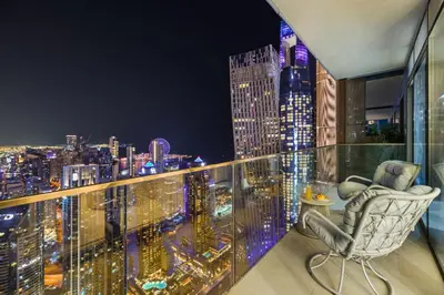 a chair on a balcony with a city skyline at night at Deluxe Marina Gate Suite with Sea and Ain Dubai View in Dubai