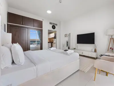 a white bedroom with a large bed and a television at Modern Comfort City Studio In Al Manara 04 in Dubai