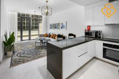 a kitchen with white cabinets and a living room at Beautiful Large 1BR Apt in District 1, MBR Minutes to Downtown in Dubai