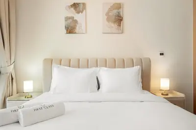 a bedroom with a white bed with two lamps at FIRST CLASS 1BR Miracle Garden View Skyz Arjan in Dubai