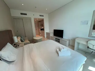 a white bedroom with a bed and a living room at Beach access, next to shopping mall in Dubai
