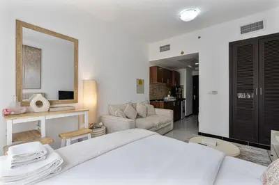 a white bedroom with a bed and a living room at Chic Studio in JVC near Stadium and Miracle Garden in Dubai