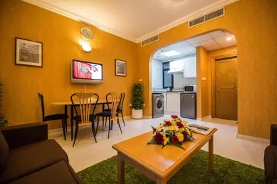 a living room with a table and a kitchen at Welcome Hotel Apartments 1 in Dubai