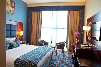 a hotel room with a bed and a desk and a window at Ramee Rose Hotel in Dubai