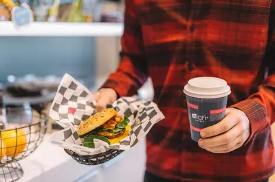 a man holding a hamburger and a cup of coffee at Aloft Me'aisam, Dubai in Dubai