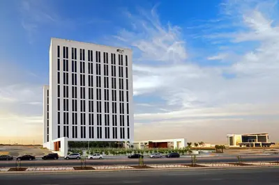 a tall white building with cars parked in a parking lot at Aloft Me'aisam, Dubai in Dubai