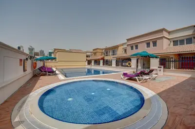 a swimming pool with chairs and umbrellas next to a building at J5 Villas Holiday Homes Barsha Gardens in Dubai