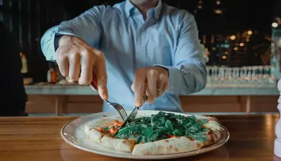 a person cutting into a pizza with a fork and knife at Studio One Hotel in Dubai