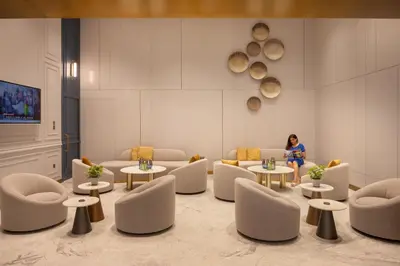 a woman standing in a waiting room with tables and chairs at Oaks Liwa Heights Hotel Suites in Dubai
