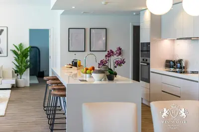 a kitchen with white cabinets and a island with bar stools at Westminster Burj Residences in Dubai