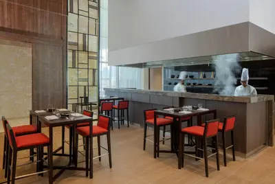 a restaurant with tables and red chairs and chefs in the kitchen at Hyatt Place Dubai Jumeirah Residences in Dubai