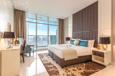 a bedroom with a large bed and a desk and a large window at Staycae Bay's Edge in Dubai