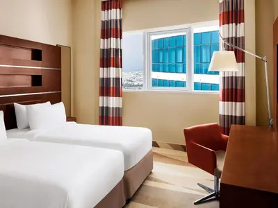 a hotel room with two beds and a desk and a window at Novotel Dubai Al Barsha in Dubai