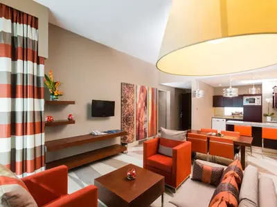 a living room with orange furniture and a kitchen at Novotel Dubai Al Barsha in Dubai